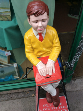 Photograph of a fiberglass statue of a seated boy whose fingers are touching the cover of a closed book.